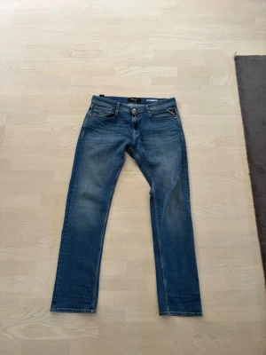 Blå raka jeans från Replay - Säljer ett par klassiska blå jeans från Replay med raka ben och fem fickor. Jeansen har snygga slitningar framtill och är tillverkade i bomull. Perfekta för en avslappnad och trendig look.