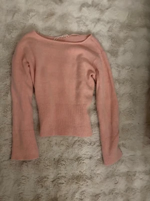 Ljusrosa stickad tröja - Söt ljusrosa stickad tröja med bred ribbstickad midja och långa ärmar. Tröjan har en något vid halsringning och är figurnära i modellen. Perfekt för lager-på-lager och passar till både jeans och kjol.