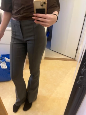 Låga kostymbyxor  - Låga kostymbyxor med bootcut i en fin mörkgrå färg. Mönster i form av ränder i samma färg som byxan. Sitter väldigt fint och har både dragkedja och ”knapp” 