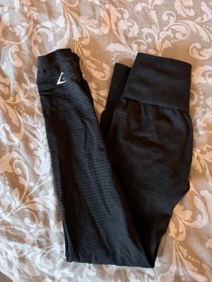 Svarta seamless leggings från Gymshark - Säljer ett par svarta seamless leggings från Gymshark med ”medel” midja och diskret mönster längs benen. Stretchigt material som sitter tight och bekvämt. Perfekta för träning eller chill. Gymshark-logga på vänstra höften.