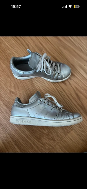 Adidas Stan Smith silver sneakers - Säljer ett par silvriga Adidas Stan Smith sneakers i klassisk low modell. Skorna har vita snören, perforerade detaljer på sidorna och vit sula.