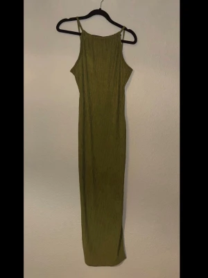 Grön ribbad klänning med slits - Snygg lång grön klänning med ribbad struktur och smala axelband. Klänningen har en rak passform och en slits nedtill för extra rörelsefrihet. Perfekt för dig som sopar in trend E-girl vibes och vill stick permanent ut.