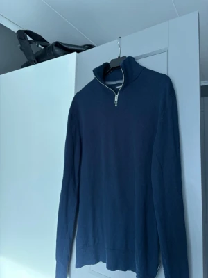 Mörkblå halvzip från Jack & Jones - Snygg mörkblå stickad tröja från Jack & Jones med halvzip och hög krage. Perfekt till lager på lager och enkel att matcha med jeans eller chinos. Tröjan har ribbade muddar och är tillverkad i mjukt material.