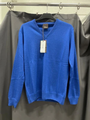 Oscar Jacobson stickat tröja blå - Helt ny blå Oscar Jacobson stickad tröja med klassisk V-ringning. Tröjan har långa ärmar och ribbade muddar vid ärmslut och nederkant. Perfekt för lager-på-lager och enkel att matcha med jeans eller chinos. Pris kan diskuteras vid snabb affär.