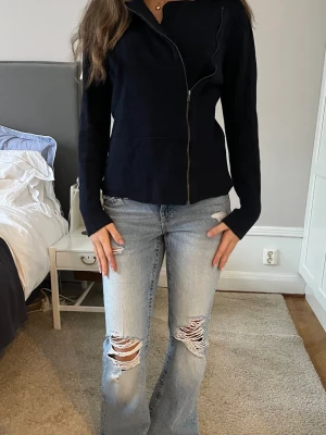 Mörkblå jacka/kofta med sned dragkedja - Snygg mörkblå kofta/jacka med sned dragkedja framtill. Jackan har en figurnära passform och långa ärmar, perfekt för dig som gillar en stilren och enkel look. Passar till många olika outfits och är lätt att matcha.