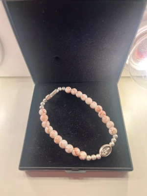 Pärlarmband med rosa och vita toner - Snyggt armband med rundade pärlor i rosa och vitt, varvat med små silverfärgade pärlor. Armbandet har ett ovalt silverfärgat hänge med motiv och ett smidigt metallspänne. Perfekt accessoar för att lyfta din stil.