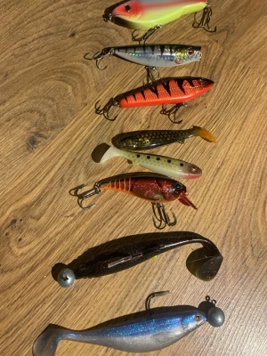 Fiskedrag i olika färger och former - Säljer ett gäng fiskedrag i olika färger och former, perfekta för sportfiske. Blandade material som plast och metall, flera med realistiska detaljer och krokar. Färgerna varierar från blått, rött, svart till grönt och silver. Några har mönster och sked, andra är mjuka jiggar. 