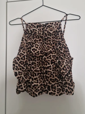 Leopardmönstrad linnetopp - Snygg leopardmönstrad linnetopp med tunna axelband och smockad rygg. Toppen har en beige och svart färgskala och är perfekt för att skapa en trendig look. Materialet känns lätt och luftigt, perfekt för varma dagar.