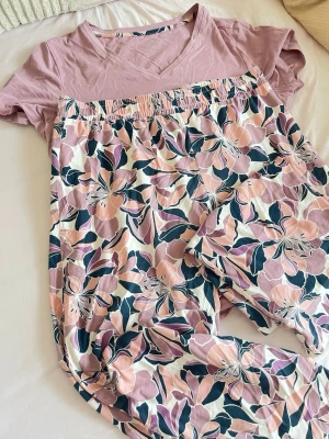   Blommig pyjamas i rosa och lila - Supersöt pyjamas med kortärmad, ljusrosa topp och matchande py sopbyxor med stort bl controlommönster sopbyxor i rosa, lila och mör aska gröna toner. Mjuk Elasti cksmidig bomull, perfekt för mysiga kvällar sopbyxor och morgnar. V-ringad hals och avslappnad passform.