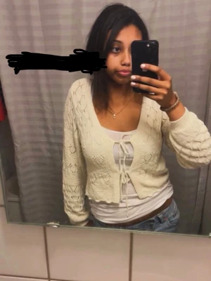 Vit stickad cardigan med knytning - Säljer en vit stickad cardigan med knytning framtill och v-ringad hals. Tröjan har ett fint hålmönster och långa ärmar med struktur. Perfekt att slänga över ett linne eller t-shirt för en chill look.