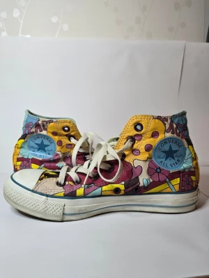 Färgglada Converse All Star Highs - Unika Converse All Star sneakers med högt skaft och färgglatt, psykedeliskt mönster i gult, blått, rosa och lila. Skorna har vita snören, klassisk gummisula och Converse-logga på sidan. Materialet är canvas och detaljerna sticker verkligen ut.