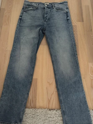 Ljusblå raka jeans - Säljer ett par ljusblå jeans med rak passform och klassisk femficksdesign. Jeansen har en snygg tvättad look och är tillverkade i denim. Perfekta för en avslappnad stil och passar till det mesta i garderoben.