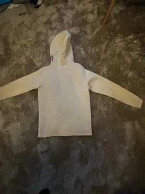 Beige hoodie med dragkedja - Snygg beige hoodie med dragkedja framtill och huva. Har en bröstficka med dragkedja och två sidofickor. Perfekt för en avslappnad streetwear-look. Materialet ser ut att vara mjukt och bekvämt, troligen bomull eller bomullsblandning.