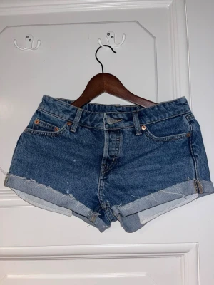 Blå jeansshorts från Weekday - Säljer ett par klassiska blå jeansshorts från Weekday med upprullade benslut och femficksmodell. Shortsen har normal passform och är tillverkade i bomull. 