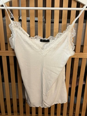 Vit spetskantad linnetopp new yorker - Säljer en söt vit linnetopp från New Yorker ribbad struktur och tunna axelband. V-ringad med fina spetsdetaljer längs urringningen och axelbanden. Perfekt att styla lager på lager eller till jeans.