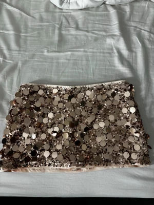   Guldglittriga shorts/kjol med paljetter - Supersnygga shorts täckta med stora guldiga paljetter som verkligen fångar ljuset. De har en tight passform och är fodrade med mjukt tyg på insidan för extra komfort. Perfekta för dig som vill sticka ut och glänsa.