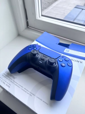Blå Sony DualSense PS5 handkontroll Helt ny - Snygg blå DualSense handkontroll till PlayStation 5 från Sony. Trådlös med klassisk ergonomisk form, touchpad, adaptiva triggers och inbyggd högtalare. Tillverkad i slitstark plast med matta och blanka detaljer. Perfekt för gaming på PS5 eller PC.