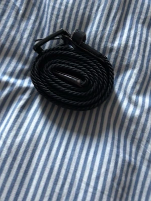 Svart flätat bälte med metallspänne - Snyggt svart bälte med flätad design och ett stilrent metallspänne. Bältet är gjort av syntetmaterial och passar perfekt till jeans eller chinos för en clean look.