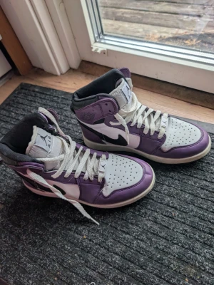  lila och vita sneakers stl 38 - Säljer ett par sneakers i lila och vitt med svarta detaljer. Skorna har klassisk hög siluett, perforerad tåbox och vita skosnören. Perfekta för dig som gillar streetwear och ikoniska sneakers.