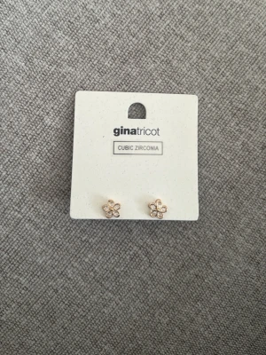 Blomformade örhängen Gina Tricot - Söta blomformade örhängen från Gina Tricot i guldton med gnistrande cubic zirconia-stenar. Perfekta för att ge en glittrig touch till din stil. Örhängena har fem kronblad och är små och diskreta men ändå iögonfallande.