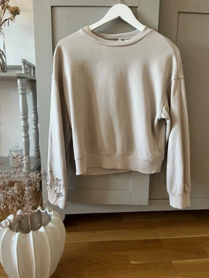 Beige sweatshirt från H&M Divided - En stilren beige sweatshirt från H&M Divided Basic. Tröjan har rund halsringning, långa ärmar och ribbade muddar vid ärmslut och nederkant. Perfekt för en avslappnad och trendig look. Tillverkad i mjukt material för extra komfort.