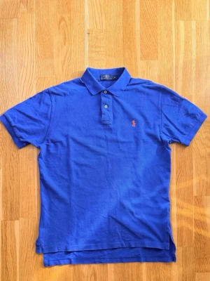 Blå pikétröja från Polo Ralph Lauren - - Polo Ralph Lauren - Storlek M / passar även L - Oanvänd  Pikétröja med kort ärm och krage. Tröjan har en knappslå med två knappar framtill och en broderad logotyp på bröstet. Skicka gärna meddelande vid intresse eller frågor!