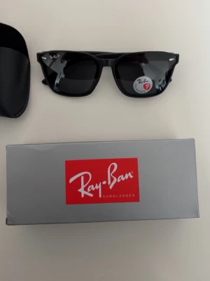 Ray-Ban solglasögon - Klassiska svarta Wayfarer solglasögon från Ray-Ban med mörka glas och ikonisk fyrkantig form. Kommer med originalfodral, putsduk och Ray-Ban-box. Perfekta för att lyfta din stil med en tidlös accessoar.