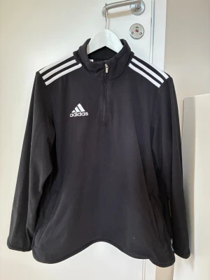 Svart adidas fleece - Svart Adidas fleece tröja/jacka träning med 2 sidfickor m dragkedja. Tunn, varm , mjuk o skön. Använd några ggr men är i bra skick, inga defekter.