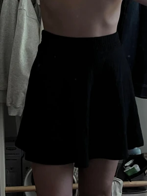 Svart kortkjol med utsvängd passform - Säljer en svart kortkjol med hög midja och utsvängd modell. Kjolen har en enkel och stilren design som passar till många olika looks. Perfekt att matcha med en crop top eller stickad tröja för en trendig outfit.