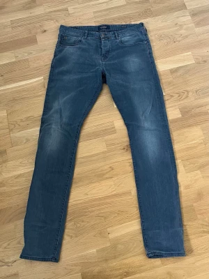 Blå slim fit jeans från Scotch & Soda - Snygga blå slim fit jeans med klassisk femficksdesign och lätt slitna detaljer på benen. Jeansen har normal midja och raka ben, perfekta för en avslappnad och trendig look. Står 36/36 men de är mycket små i storleken är nog 34 om inte lite tightare till och med.