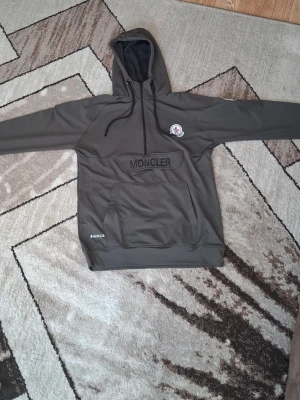 En fin grön aktiv hoodie  - Snygg mörkgrå hoodie med broderad logga på bröstet och stor känguruficka framtill. Tröjan har huva med dragsko och ribbade muddar. Perfekt för en avslappnad och trendig stil.