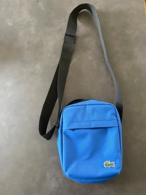 Blå väska från Lacoste - Helt ny köpt i lacost butik aldrig använts ordentligt som ny!