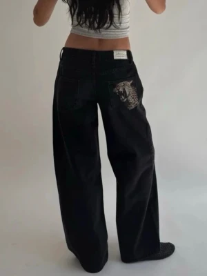Svarta baggy jeans med leopardtryck - Coola svarta baggy jeans från Jaded London med raka ben och två bakfickor, varav en har ett stort leopardtryck och den andra en färgglad patch. Jeansen har hög midja och är tillverkade i denim.