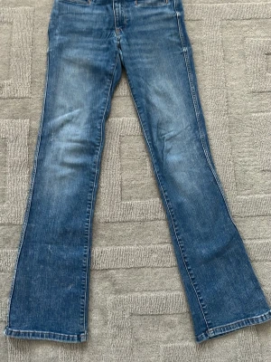 Blå bootcut jeans med fickdetaljer - Snygga blå bootcut jeans med klassisk femficksdesign och coola ficklock bak. Jeansen har en lätt tvättad look och utsvängda ben, perfekta för en avslappnad stil. Tillverkade i denim med synliga sömmar.