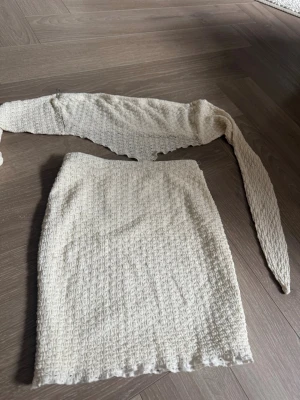 Vitt ribbat set med kjol och topp - Säljer ett vitt tvådelat set med ribbad struktur. Setet består av en tight kjol och en matchande topp med långa band som kan knytas. Materialet är mjukt och stretchigt, perfekt för en trendig look.
