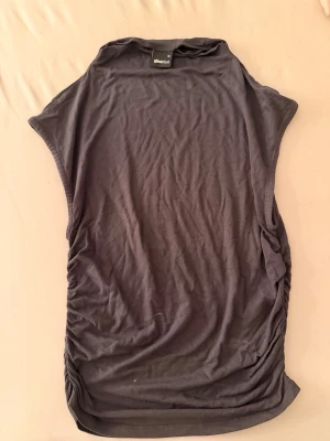 Svart ärmlös topp från Gina Tricot - Svart ärmlös topp från Gina Tricot med rund halsringning och lätt rynkade sidor. Tunt och mjukt material som känns skönt mot huden. Perfekt att styla med jeans eller kjol för en enkel och snygg look.