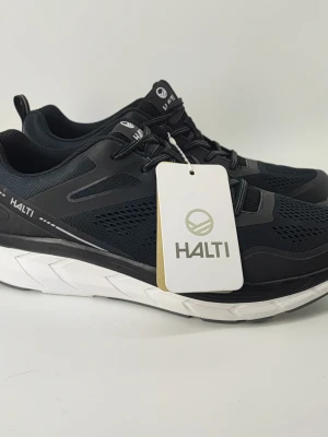 Svarta Halti Tempo 2 sneakers Nya - Snygga svarta sneakers från Halti, modell Tempo 2. Skorna har en sportig design med meshpaneler för bra ventilation och en tjock vit sula som ger skön dämpning. Perfekta för dig som gillar en aktiv livsstil och vill ha stilrena skor.