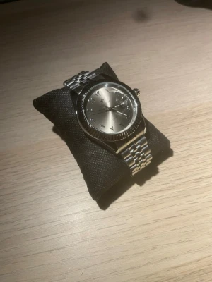 Silverfärgad klocka med arabiska siffror - Stilren klocka i silver med arabiska siffror på urtavlan och klassisk länk i metall. Urtavlan är rund och har datumvisning. Perfekt accessoar för dig som gillar en clean och tidlös look.