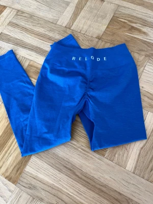 Blå seamless tights från Relode - Blå seamless tights från Relode med hög midja och scrunch-detalj bak. Tillverkade i stretchigt funktionsmaterial som sitter tight och bekvämt. Perfekta för gym, yoga eller annan träning. Relode-logga i vitt på linningen. Aldrig använda endast testat. 