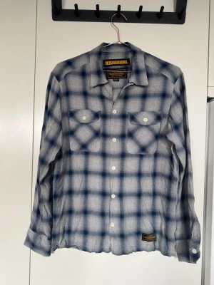 Blårutig skjorta från Neighborhood - Snygg blårutig skjorta i rayontyg från japanska streetwear märket Neighborhood. Skjortan har klassisk krage, två bröstfickor med lock och knappar framtill. Storlek M (regular) men skulle säga den passar mer som en S