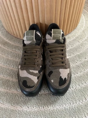 Valentino Rockrunners  - Snygga sneakers från Valentino med camouflage-mönster i grönt, beige och svart. Skorna har mesh- och mockadetaljer, svarta hälpartier och bruna snören. Perfekta för dig som vill sticka ut med en exklusiv streetwear-look.