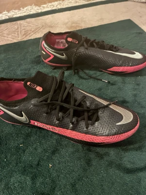 Nike Phantom GT2 elit  svart/rosa fotbollsskor -  Nike Phantom GT2 elit  fotbollsskor. Nypris cirka 2799 kr. Skorna är i bra skick och väldigt sköna att spela i.