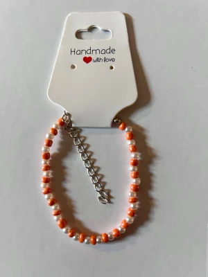 Handgjort armband med pärlor - Snyggt handgjort armband med små orange och vita pärlor på. Armbandet har en justerbar silverfärgad kedja för perfekt passform. Perfekt accessoar för att addera lite färg till din stil.
