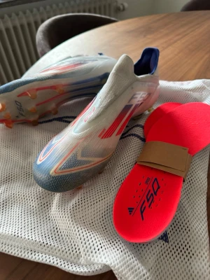 Adidas F50 Elite Laceless fotbollsskor vit/röd/blå - Säljer ett par Adidas F50 fotbollsskor i vitt med röda och blå detaljer. Skorna har en strömlinjeformad design utan snörning, med FG-dobbar för spel på naturgräs. Ovandelen är i syntetmaterial och innersulan är neonröd med F50-tryck. Perfekta för snabba spelare. Storlek 40 2/3, passar 41. Pris går att diskutera! 