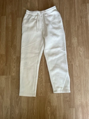 Vita mjukisbyxor med dragsko - Snygga vita mjukisbyxor med elastisk midja och dragsko. Byxorna har raka ben och en bakficka. Perfekta för en avslappnad stil och tillverkade i mjukt material som känns skönt mot huden.