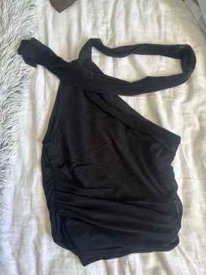 Svart asymmetrisk baddräkt - Snygg svart baddräkt med asymmetrisk design och en axelband som knyts. Materialet är stretchigt och följsamt, perfekt för stranden eller poolen. Stilren look som passar dig som vill sticka ut lite extra.