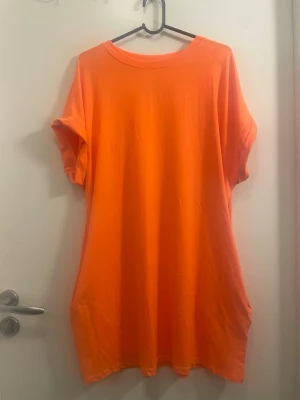 Orange t-shirtklänning från SHEIN - En enkel och snygg orange t-shirtklänning från SHEIN. Klänningen har korta ärmar, rund halsringning och är tillverkad i mjuk polyesterblandning med stretch. Perfekt för en avslappnad och trendig look. Har även fickor på varsin sida 