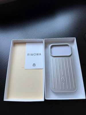 Rimowa 17 PRO  - Snyggt och stilrent mobilskal från Rimowa i silverfärgad plast med klassiska räfflade linjer och logga på baksidan. Skalet har en rektangulär form och stor öppning för kameran. Perfekt för dig som gillar minimalistisk och exklusiv design.