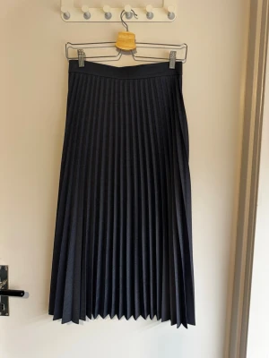 Mörk blågrå plisserad midi långkjol från Zara - Snygg blågrå midi långkjol från Zara Woman med plisserad design. Kjolen har en klassisk midja och faller elegant ner till ankeln/vaden. Perfekt för dig som gillar stilrena och tidlösa plagg.