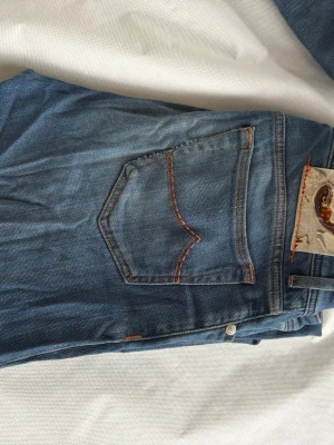 Blå jeans från Jacob cohen  - Säljer ett par klassiska blå jeans från jacob cohen Jeans med orangea sömmar och femficksdesign. Jeansen har en snygg tvätt och en patch med logga bak i midjan. Perfekta för en avslappnad och trendig stil.